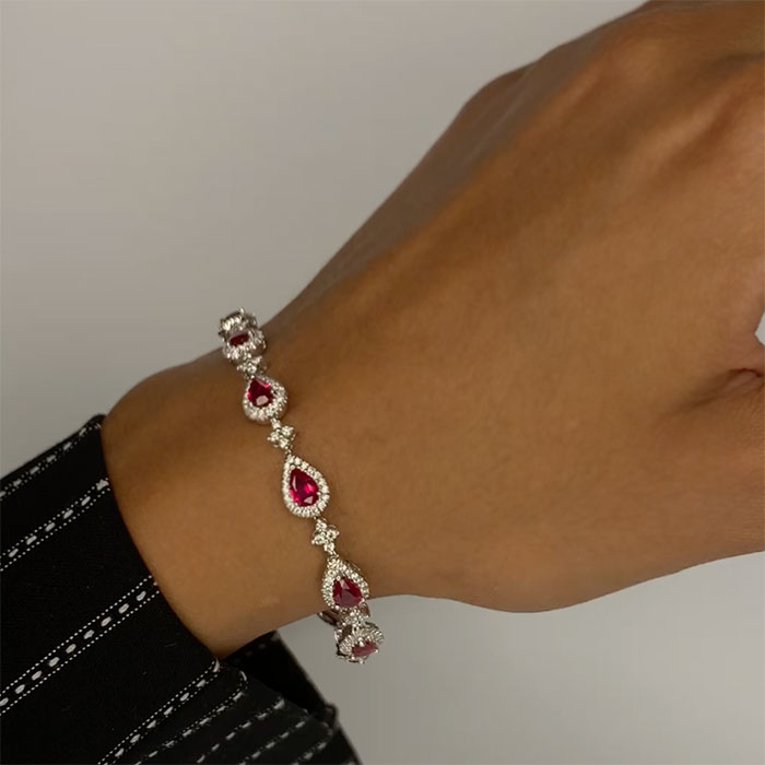 person wearing a pear shaped ruby bracelet with diamonds in white gold