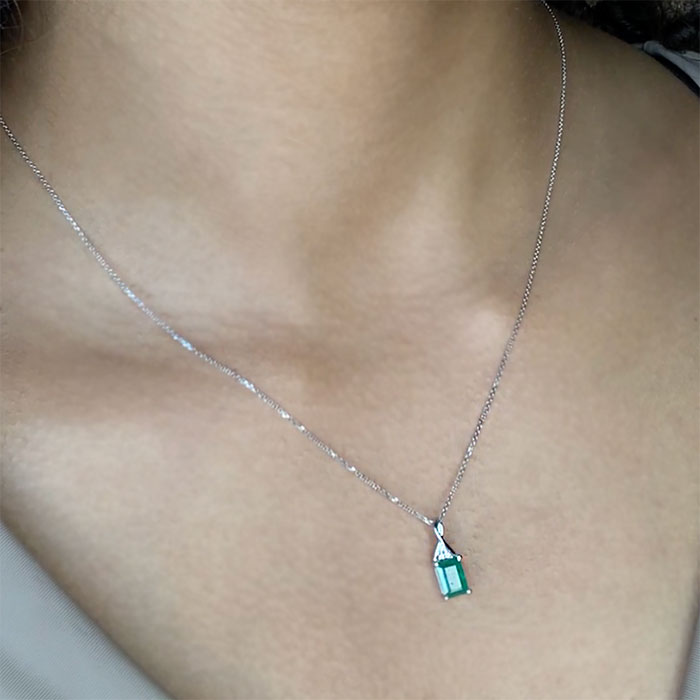 person wearing an emerald cut emerald pendant